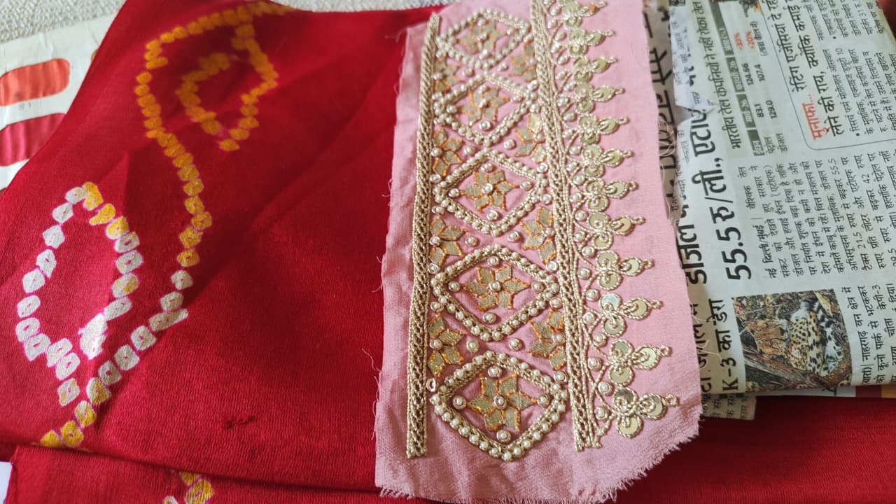 A close view of a pink embroidered strip beside a red patterned fabric.